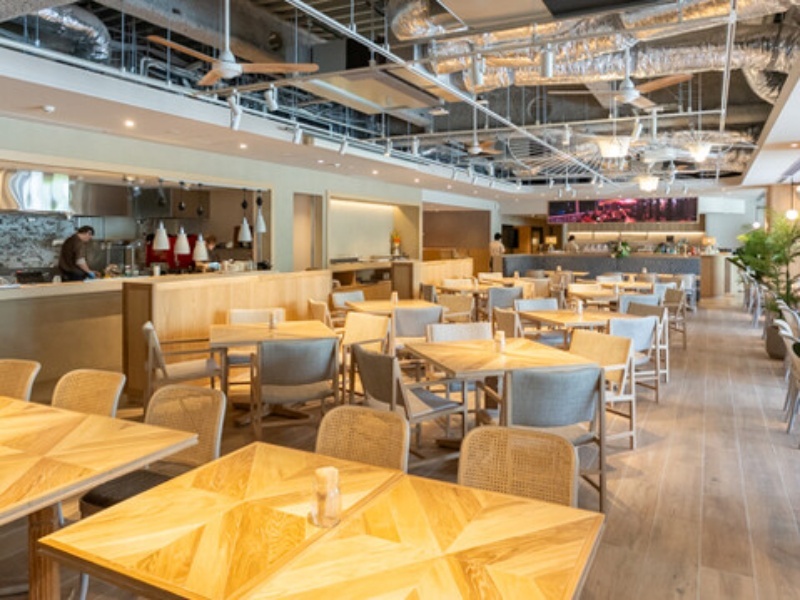 木目テーブル・ラタンチェアが並ぶナチュラルリゾートな店内。天井も高く、広々しているので、圧迫感を感じることなくお過ごしいただけます。